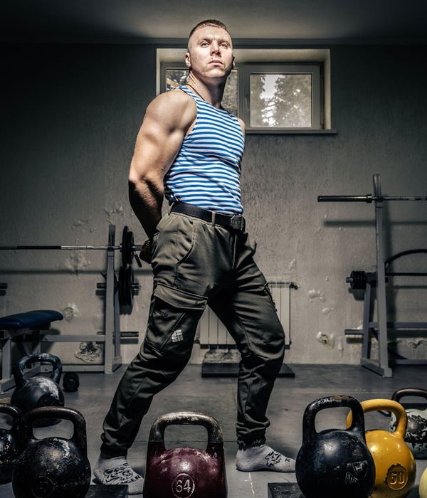 Muscular man performing heavy kettlebell swings in a dark gym setting